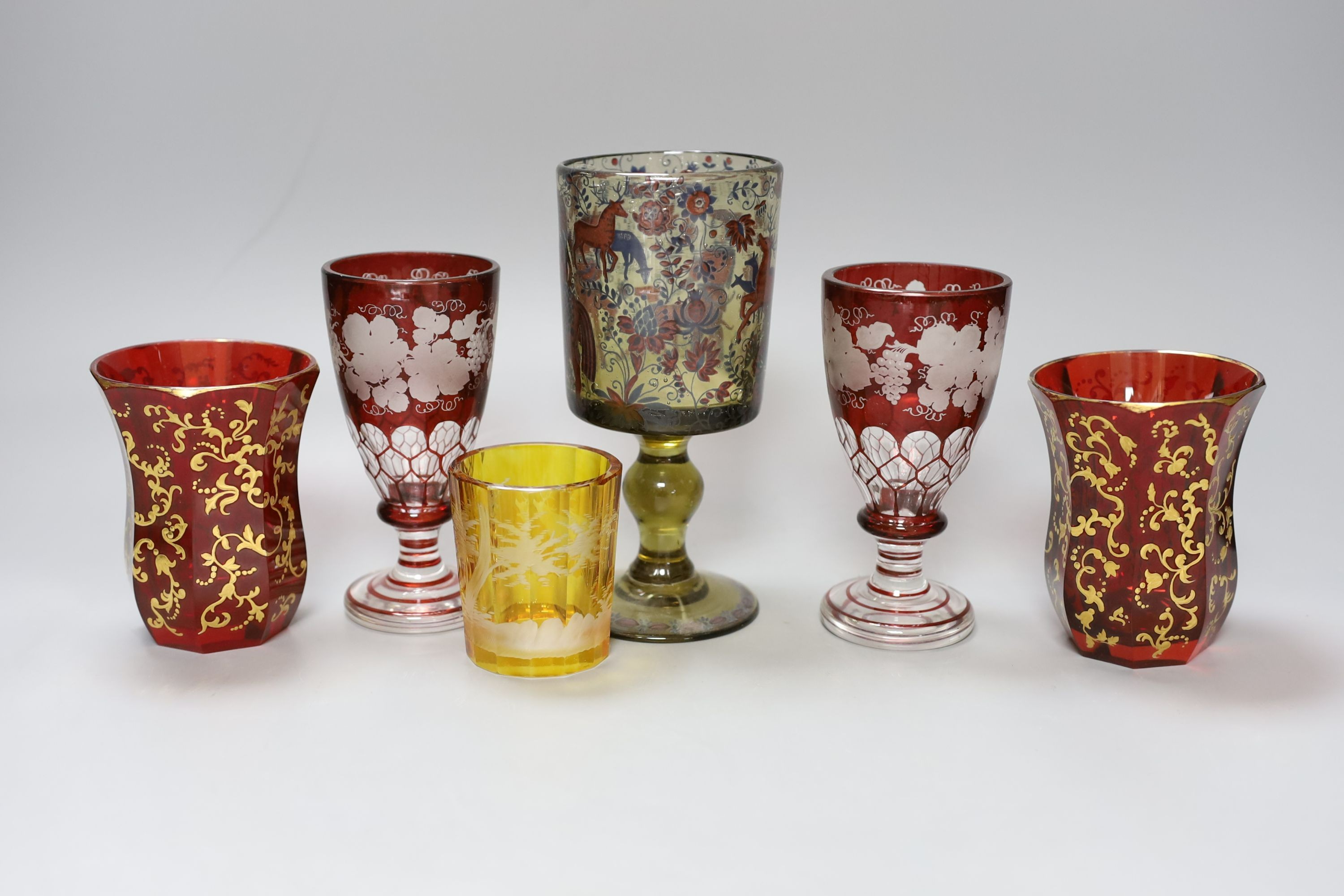 A group of Bohemian coloured glass, including a pair of vine-engraved ruby-flashed wine glasses, pair of gilded ruby glass beakers, a stag engraved, amber-flashed beaker and a Historismus goblet, 17cm